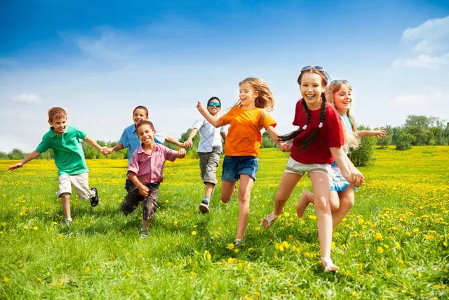 rs=w_640 Children running and holding hands in a sunny field with green grass and yellow flowers.