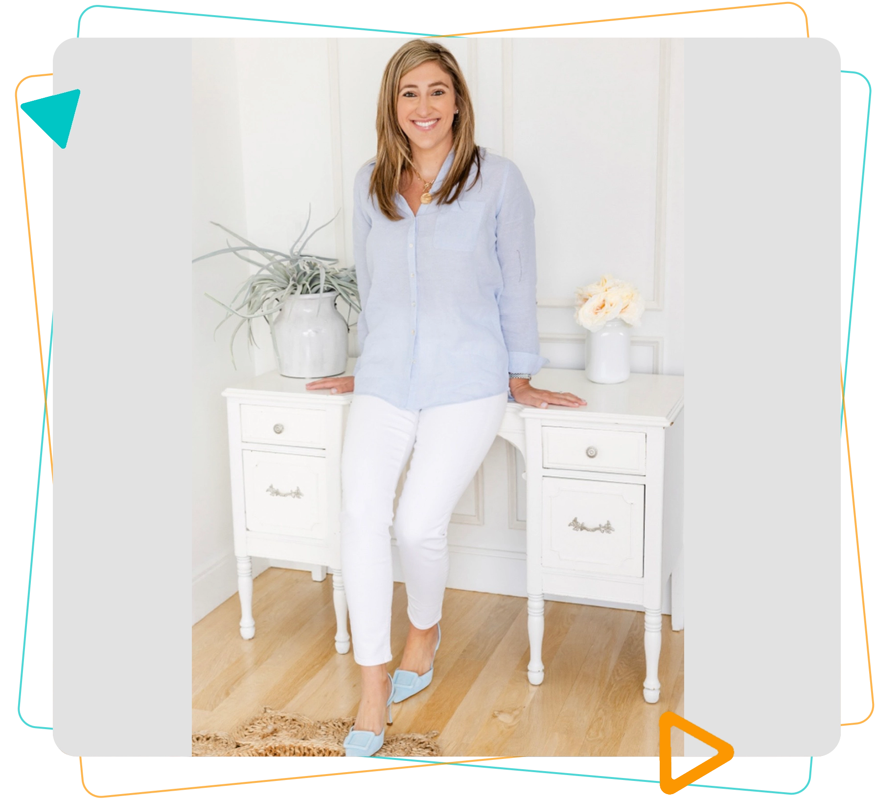 A woman stands in front of a white desk, wearing a light blue shirt, white pants, and blue shoes. The desk holds two vases with plants and flowers.